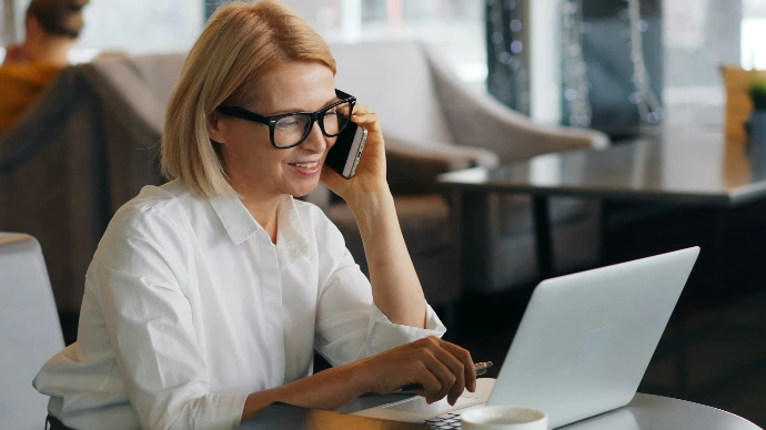 a woman talking on a cell phone while using a laptop